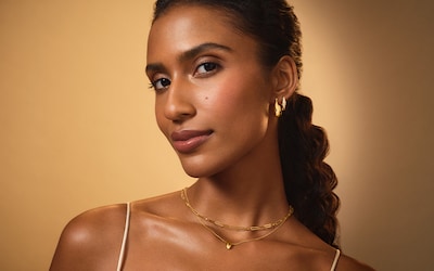 Image of Goldsmiths model wearing yellow gold jewellery on bronze background. Tap to shop new in jewellery image
