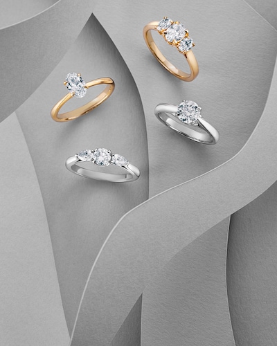 Grey background with yellow gold and platinum diamond engagement rings. Tap to shop all Mappin & Webb Engagement rings. Discover beautifully designed rings that capture the brilliance of your story together. image