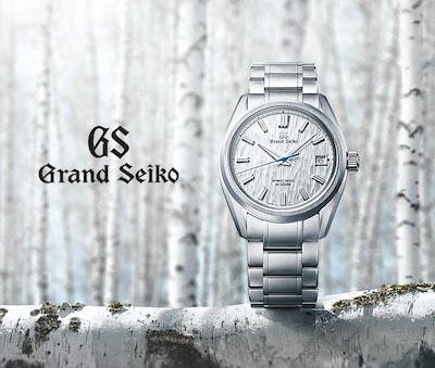 A sleek Grand Seiko watch with a textured silver dial is displayed against a serene birch tree background. image