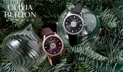 Two elegant Olivia Burton watches, one with a black face and the other in deep purple, displayed among pine branches and glass ornaments with Olivia Burton Logo Olivia Burton logo image
